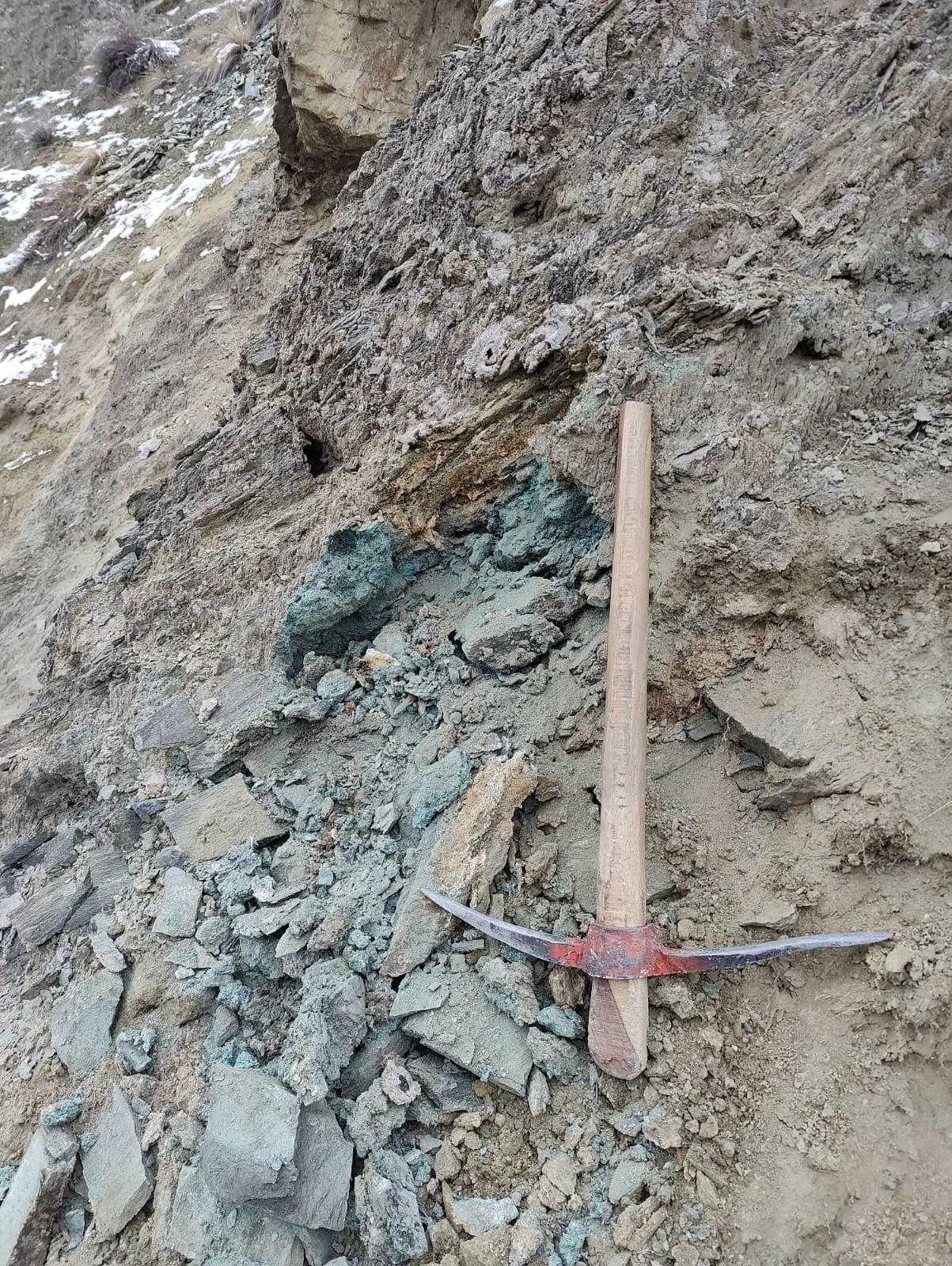 Green copper-oxide ore exposed at the outcrop, with a pickaxe for scale